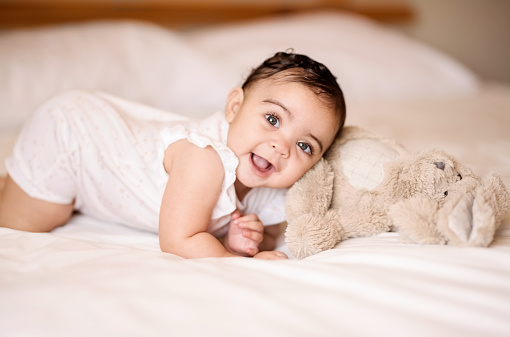 Shot of a cute baby girl on bed playing with a teddy bear