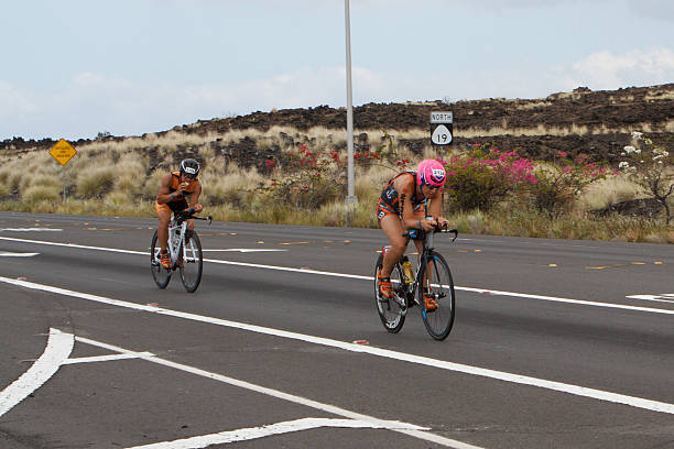 Kona Ironman Triathalon Kona, Hawaii, USA - October 11, 2014: Kona Ironman athlete #2134, Nicole Pressprich (USA), during the return bike portion of the annual Kona Ironman triathalon, followed by #2156, Anthony Chan (USA), loading up on carbs. neicebird stock pictures, royalty-free photos & images