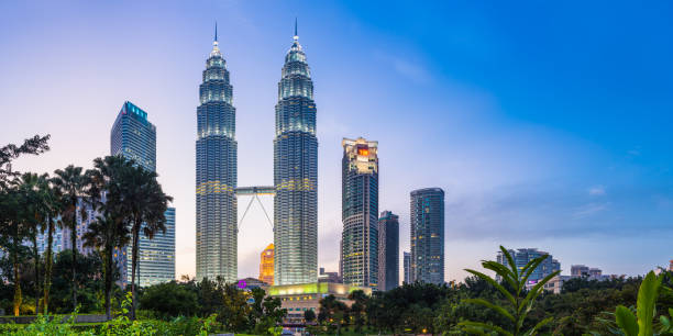 Kuala Lumpur skyscrapers glittering at sunset KLCC Park panorama Malaysia The iconic twin spires of the Petronas Towers glittering against the blue dusk sky above the ponds of KLCC Park and Suria KLCC in the heart of Kuala Lumpur, Malaysia's vibrant capital city. bukit bintang stock pictures, royalty-free photos & images