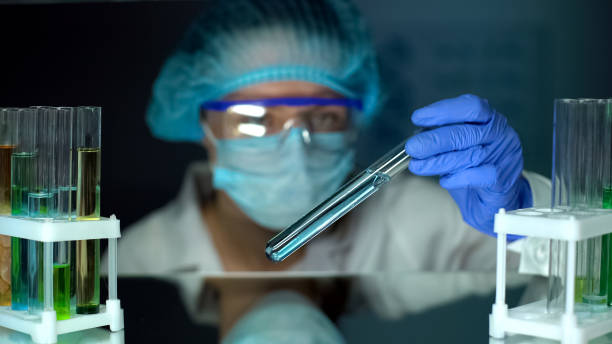 Lab worker looking at tube with blue liquid, detergents, perfumery production stock photo