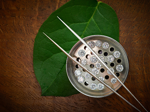 Lab-grown ethical diamonds in sieve on wooden background with green leaf to symbolise green credentials.