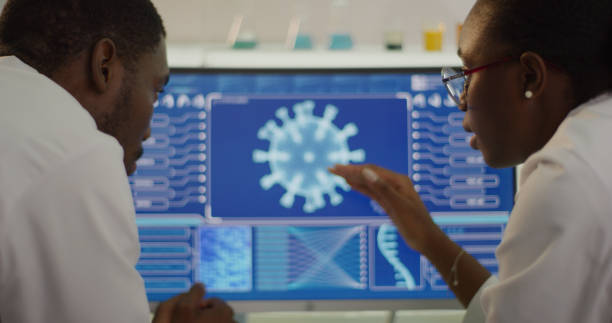 Laboratory equipment and computers. Coronavirus models on screens. African ethnicity scientists discussing. Close up on hands and screens. Pointing details stock photo
