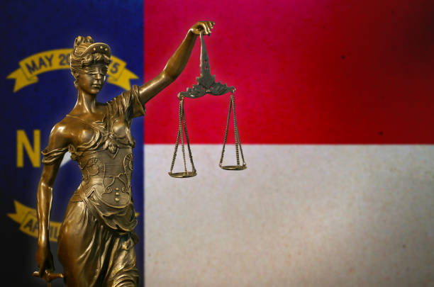 Lady Justice before a flag of North Carolina Close-up of a small bronze statuette of Lady Justice before a flag of North Carolina. north carolina us state photos stock pictures, royalty-free photos & images