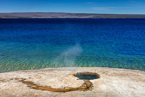 Thumb geyser basin with smoke near West Thumb lake with blue water of Yellowstone National Park, Wyoming, USA.