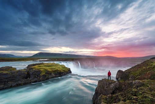Godafoss waterfall. Beautiful landscape in Iceland. Man in red jacket standing on the rock and looking at the dawn