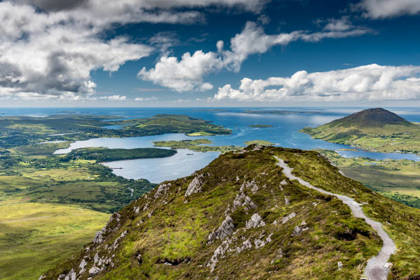 Landscape of the coast of Connemara The hiking trail at the top of Diamond Hill in Connemara National Park, Ireland. Behind, the sun plays with the clouds reflected in the sea. connemara stock pictures, royalty-free photos & images