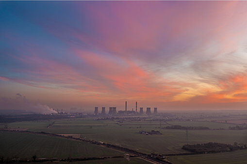 A long range landscape view of a coal fired power station generating non renewable electricity under a dramatic sky at sunset
