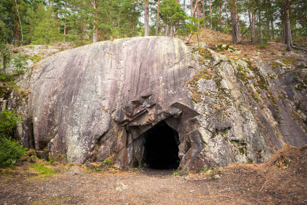 Landscape with cave and forest. Scenic entrance to cave. Rock wall with a dark hole. Spro, Mineral historic mine. Nesodden Norway. Nesoddtangen peninsula. Exterior of the cave on Norway coast. Stone wall with dark entrance to cave inside the wood. grotto cave stock pictures, royalty-free photos & images