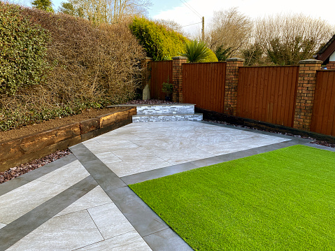 Landscaped garden with and artificial lawn and ceramic paving slabs in contrasting grey colours.  No people.