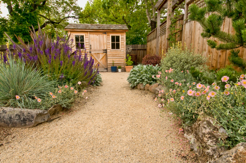 beautifully landscaped backyard with small wooden shed, fence and pathway