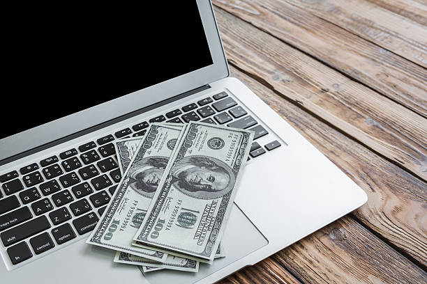 laptop and one hundred dollar banknotes on wooden table. stock photo