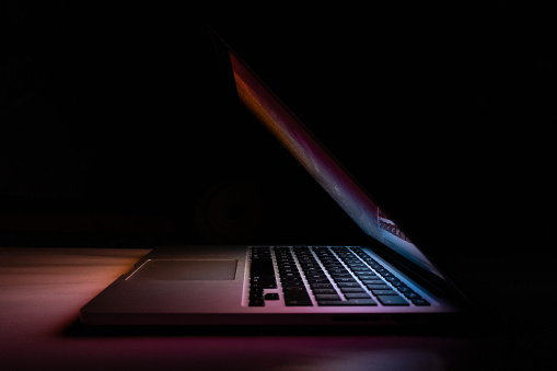 a macbook pro 15 inches half closed from the side in the dark