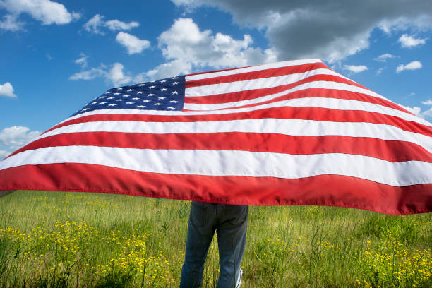 Large American flag blowing in wind in grass field in rural country stock photo