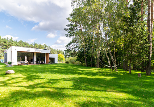 Spacious backyard next to a forest with green lawn of a modern private house.