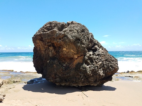 large boulder or rock on the beach with ocean and waves