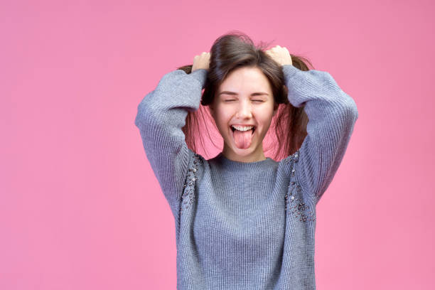 large detailed Studio portrait on pink background young Caucasian girl in a gray sweater, closed eyes and with its tongue hanging out. Her hands grip the hair as braids. large detailed Studio portrait on pink background young Caucasian girl in a gray sweater, closed eyes and with its tongue hanging out. Her hands grip the hair as braids. big smile emoji stock pictures, royalty-free photos & images