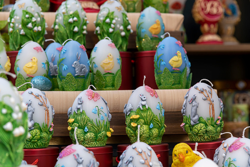 Group of large colorful and decorated egg shaped easter candles standing on store shelfs. Selective focus. Easter souvenir theme.