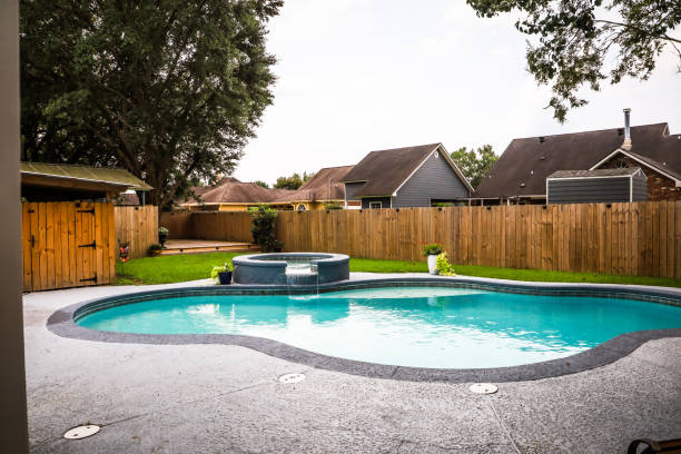 A large free form gray grey accent swimming pool with turquoise blue water in a fenced in backyard in a suburb neighborhood. stock photo