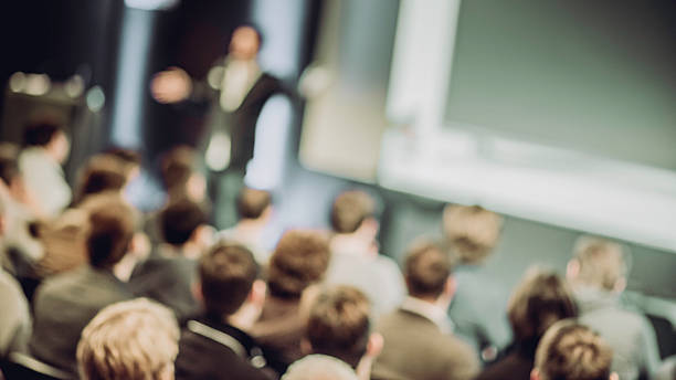 Large Group of People Listening to a Presentation Defocused shot of crowd in the lecture hall. Purposely blurred with a lens. entertainment event stock pictures, royalty-free photos & images
