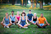 Calm people meditating in the field surrounded by greenery.  