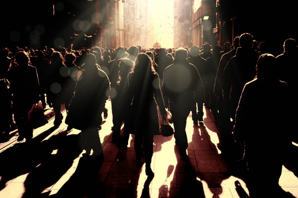 Large group of silhouetted people walking on busy street stock photo