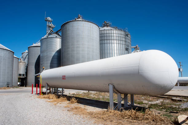 large, long white anhydrous ammonia tank with corn grain bins in background at grain elevator company stock photo