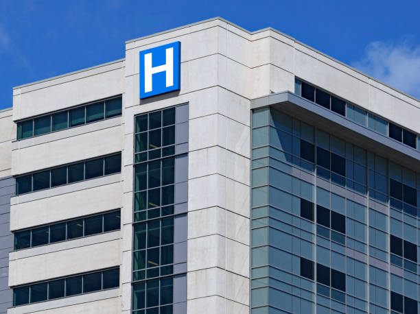 large modern building with blue letter h sign for hospital - hospital imagens e fotografias de stock