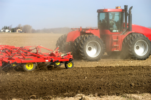 A large articulating tractor cultivating a farm field in preparation for spring seeding. (note - some dust in the air)Similar images.