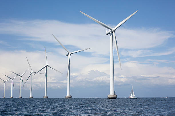 Large white windmills in the sea with a sailboat stock photo