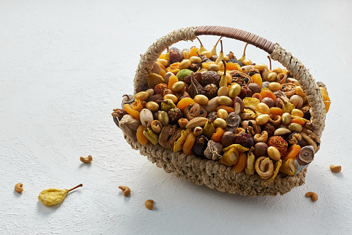 Large wicker basket filled with nuts and dried fruits on a white background