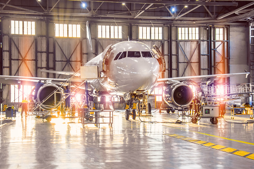 Large-scale inspection of all aircraft systems in the aircraft hangar by worker mechanics and other specialists. Bright light outside the garage door
