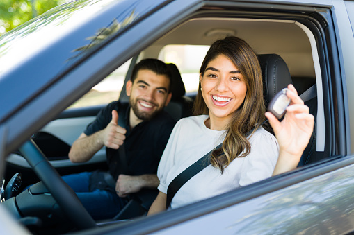 Gorgeous woman showing her keys after buying a new car. Excited couple giving a thumbs up to their rental car