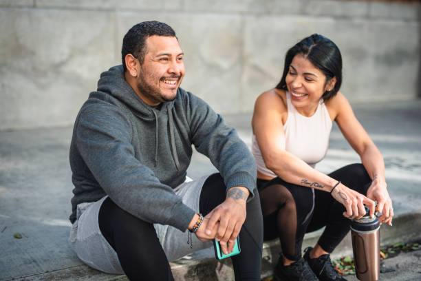 Latin man and woman athlete sitting on the pavement and taking a break stock photo