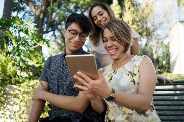 Latin mother using digital tablet outside with her children stock photo