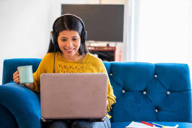 Latin woman works from the sofa at home Latin woman of average age of 25 years dressed casually is sitting on the sofa at home working using her tablet and headphones at work from home given the quarantine by the covid 19 columbian woman stock pictures, royalty-free photos & images