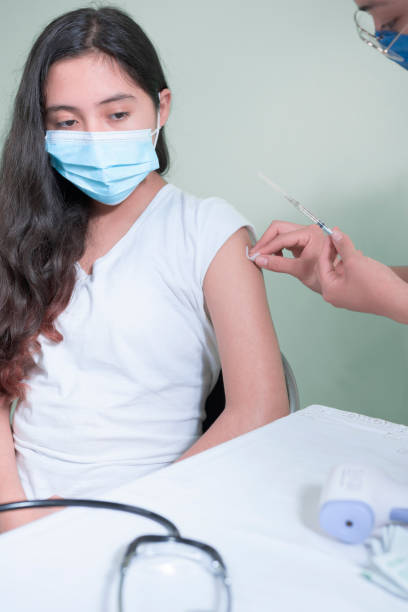 Latina female doctor takes an alcohol swab and places it on the arm of a Hispanic adolescent to disinfect the vaccine area stock photo