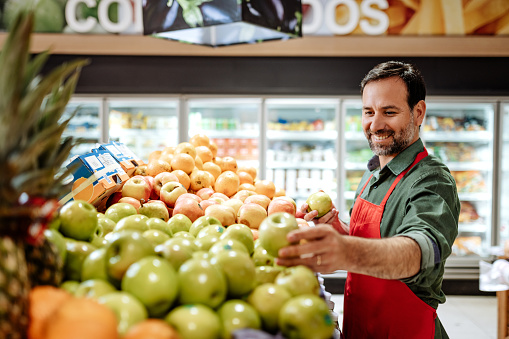 Latino employee in supermarket arranging fruit stack