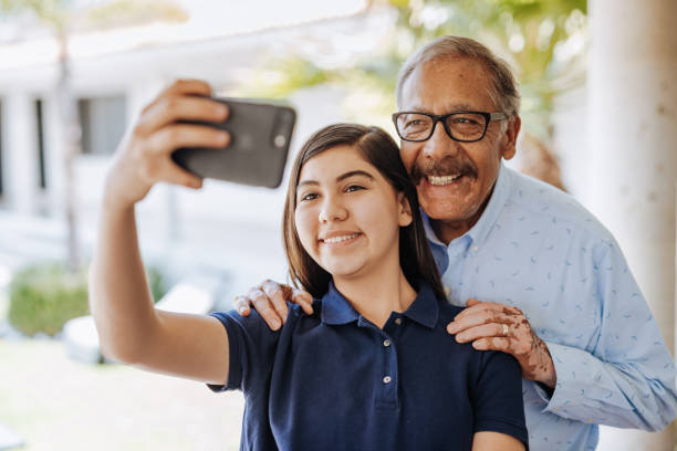 Latino Grandfather and teenage girl taking selfie Senior Latino couple enjoying weekend with their grandchildren and family at home in summertime. mexican teenage girls stock pictures, royalty-free photos & images