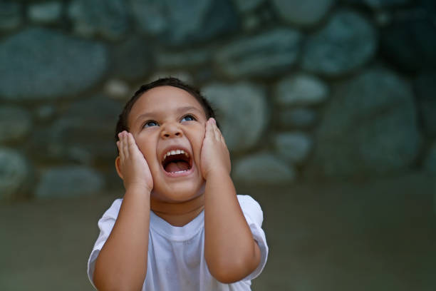 Latino preschooler overwhelmed with happiness holds his face with both hands and screams really loud. stock photo