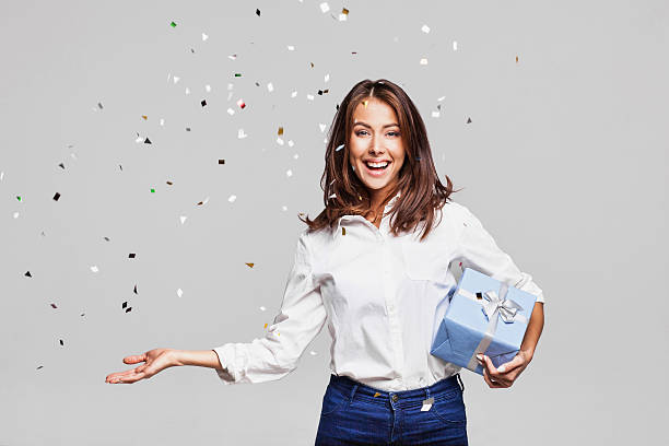 Laughing girl with falling confetti at party Beautiful woman with confetti and gift box at party on gray background Birthday Package stock pictures, royalty-free photos & images
