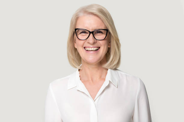 laughing mature businesswoman wearing glasses posing on grey studio background - medial object imagens e fotografias de stock