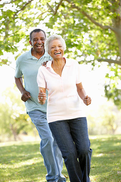 Laughing senior African American couple running through park Senior African American Couple Running In Park And Laughing old black couple in love stock pictures, royalty-free photos & images