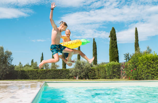 Laughing Son with Father in the inflatable ring having fun on a merry vacation. Cheerful fooling around they jumping to the swimming pool. Family time, fatherhood, or childhood concept image. stock photo