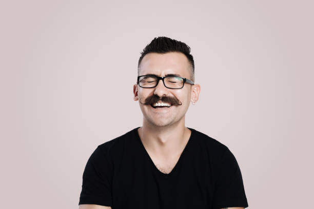Laughing young man with mustache Young male with glasses and mustache, grey background, studio shot, laughing big smile emoji stock pictures, royalty-free photos & images