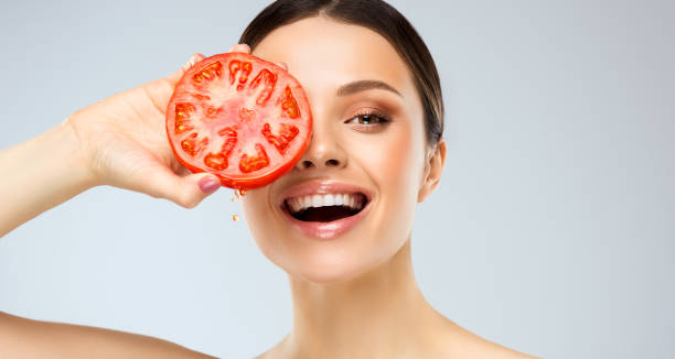 Laughing young woman is holding fresh, ripe tomato in the hand. Happiness on the face with toothy smile. stock photo