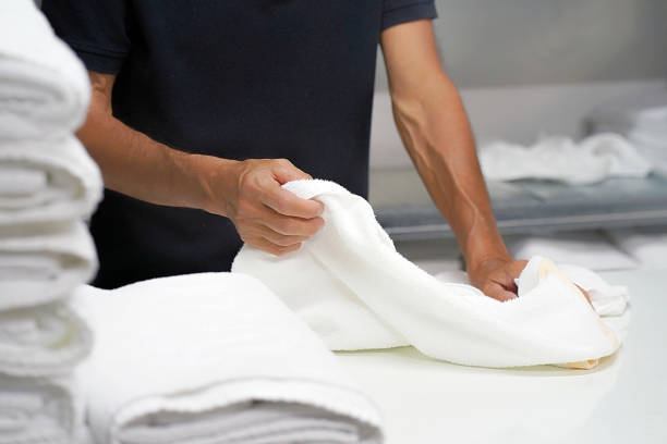 Laundry hotel. A man lays out a white towel. Hands of caucasian male laundry hotel worker folds a clean white towel. Hotel staff workers. Hotel linen cleaning services. laundromat photos stock pictures, royalty-free photos & images