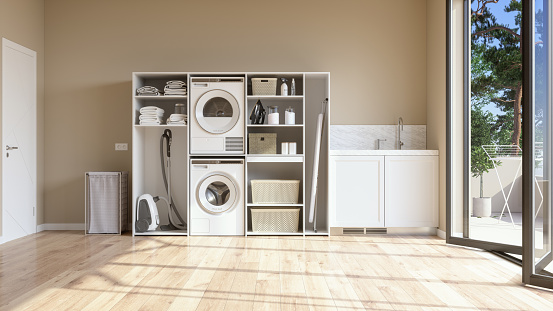 Laundry Room With Beige Wall And Parquet Floor With Washing Machine, Dryer, Laundry Basket And Folded Towels In The Cabinet.