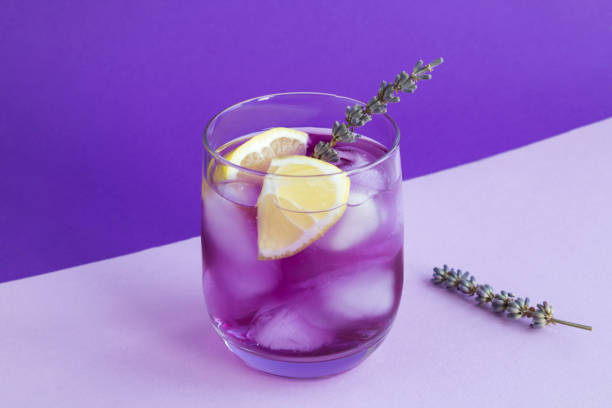 Lavender lemonade with ice and  lemon in the drinking glass on the purple background. Close-up. stock photo