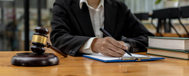 A lawyer sits in his office, on a table with a small hammer to beat the judges desk in court. and justice scales, lawyers are drafting a contract for the client to use with the defendant to sign. stock photo