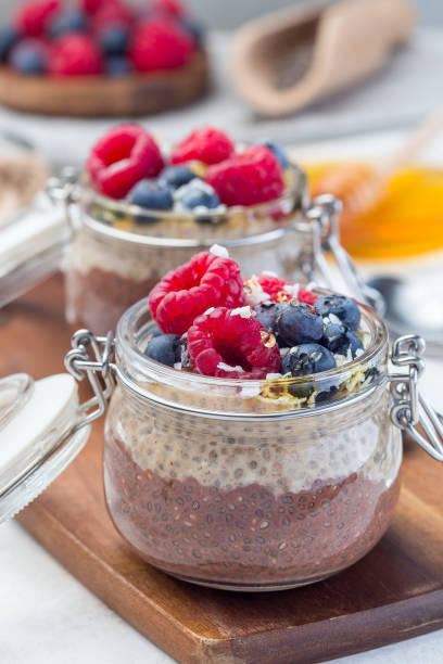 Layered chocolate and peanut butter chia seed pudding in jar, garnished with raspberry, blueberry, honey and coconut flakes, vertical stock photo